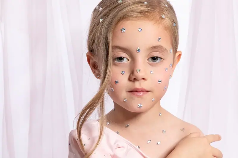 Close-up portrait of a young girl with sparkles on her face against a soft pink backdrop