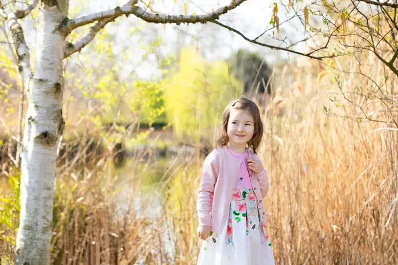 Girl in a pink top standing beside a birch tree by a lake