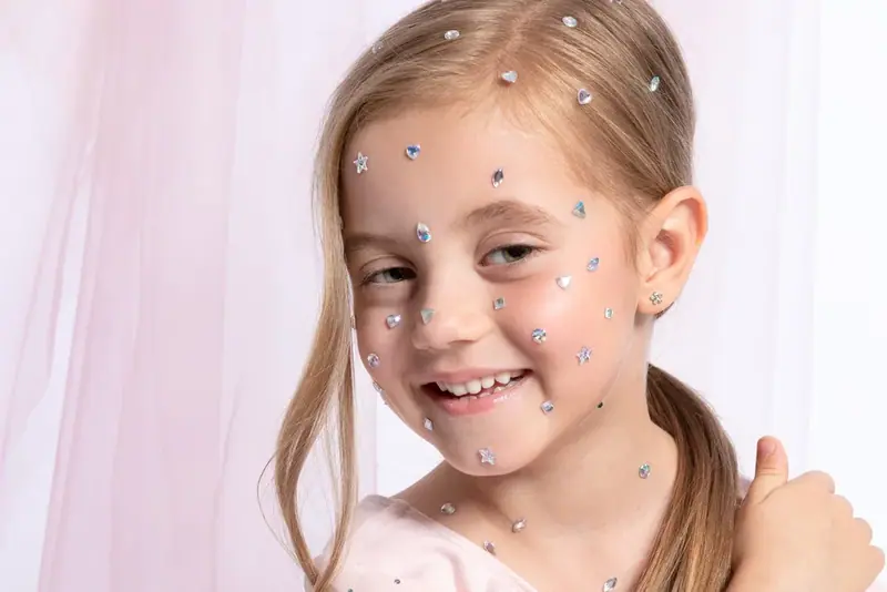 Smiling girl with sparkles on her face against a pink backdrop