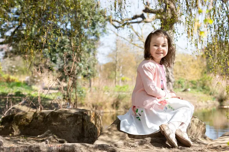 Girl in a white dress sitting on a rock by a lake under a tree