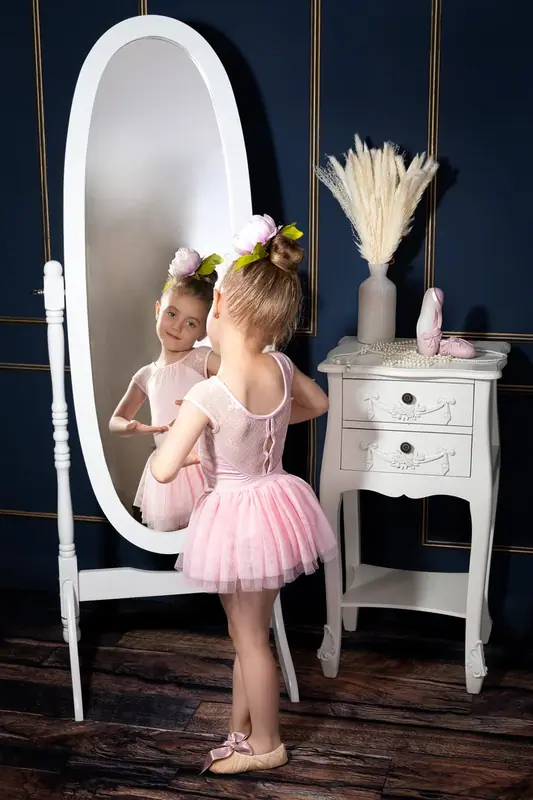 Girl in a pink tutu at a white dressing table with a tall oval mirror
