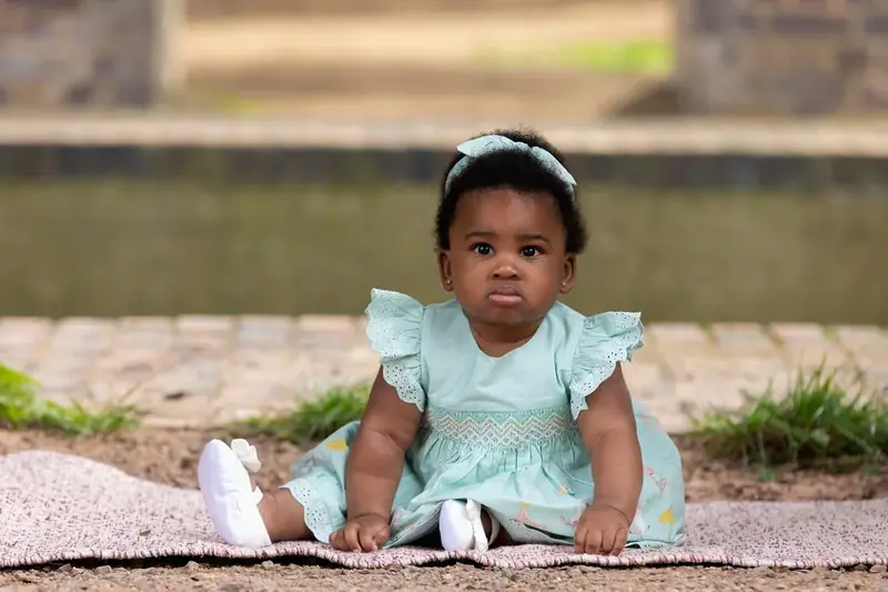 Baby girl in a mint dress sitting on a stone wall outdoors