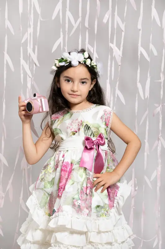 Girl in a floral dress and flower crown holding a small pink camera