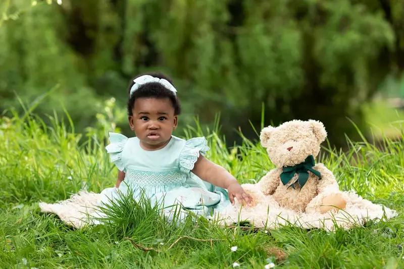 Baby in a mint dress sitting on the grass with a large teddy bear
