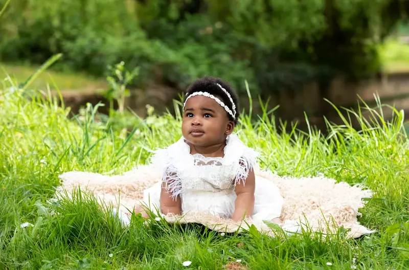 Baby girl in a white dress sitting on a fur rug on the grass