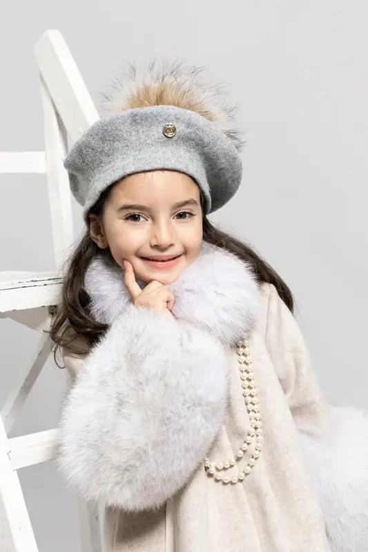Girl in a grey beret and white fur muff smiling, white background