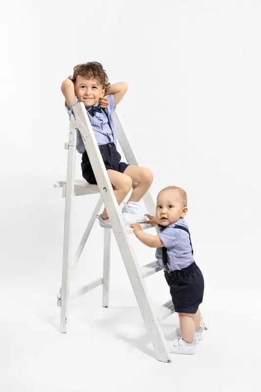 Two young children climbing a white step ladder, white background