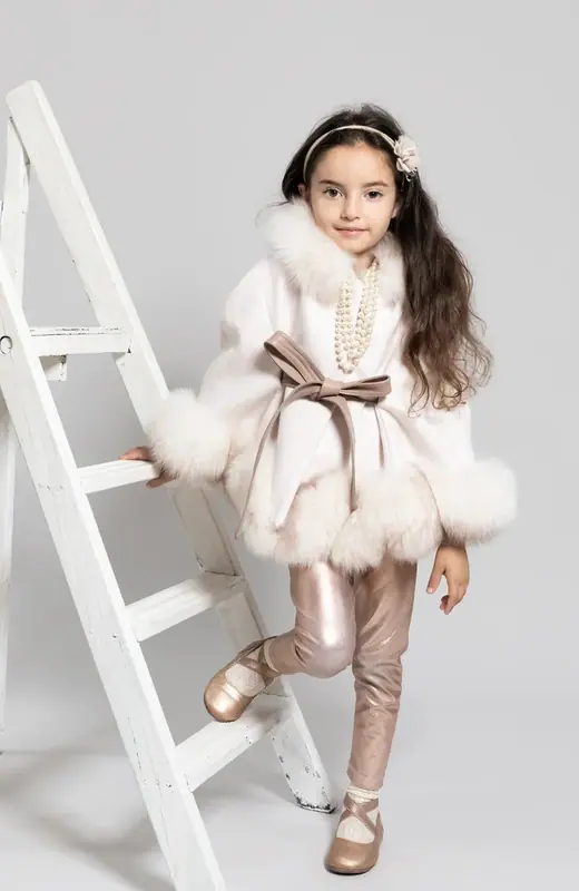 Girl in a fur-trimmed coat standing on a white step ladder
