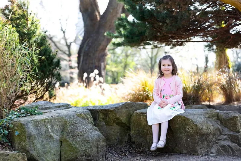 Girl in a pink dress sitting on a rock under a tree in a park