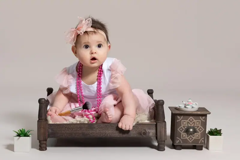 Baby girl in a pink dress and headband sitting on a small wooden bench