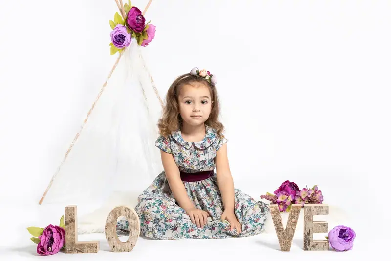Girl in a floral dress sitting under a white teepee beside wooden letters spelling LOVE
