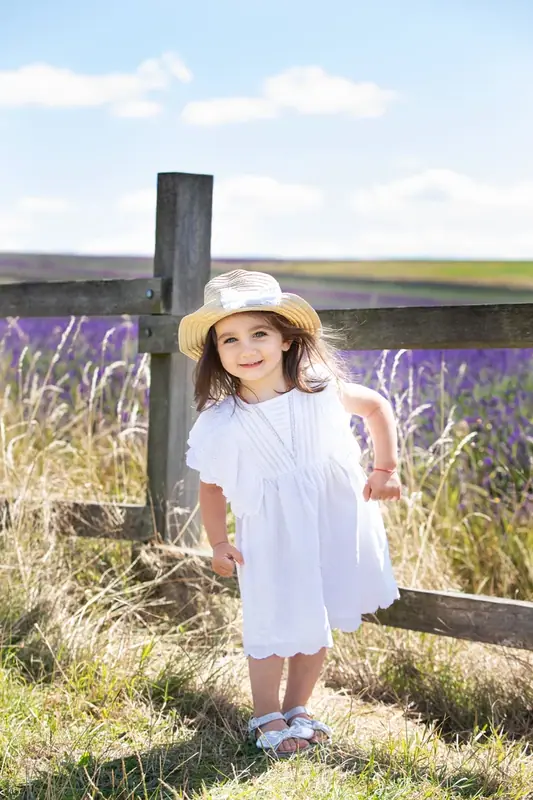 Girl in a white dress and sun hat leaning on a wooden fence