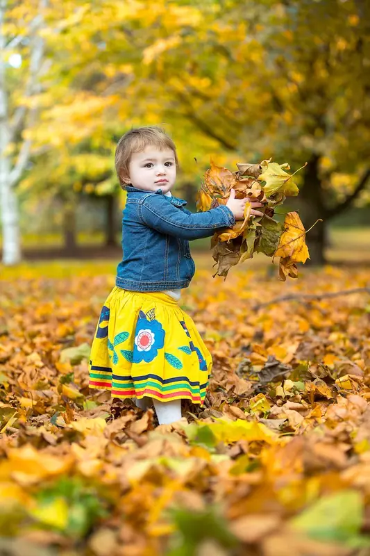 Toddler in a denim jacket playing with autumn leaves