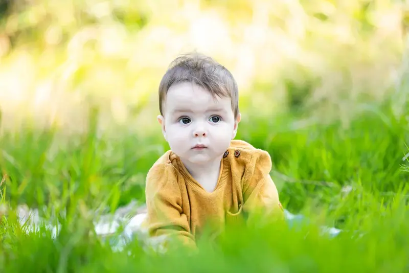 Baby in a yellow cardigan crawling on the grass