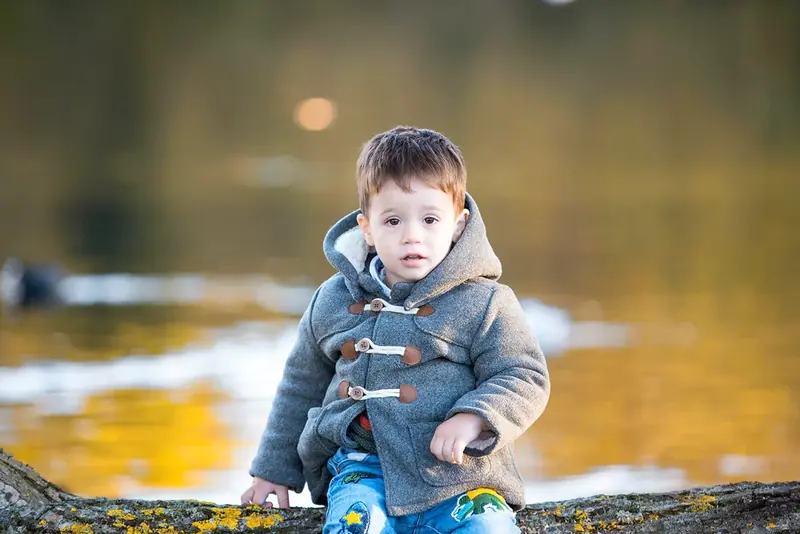 Toddler in a grey duffle coat crouching at the edge of a lake