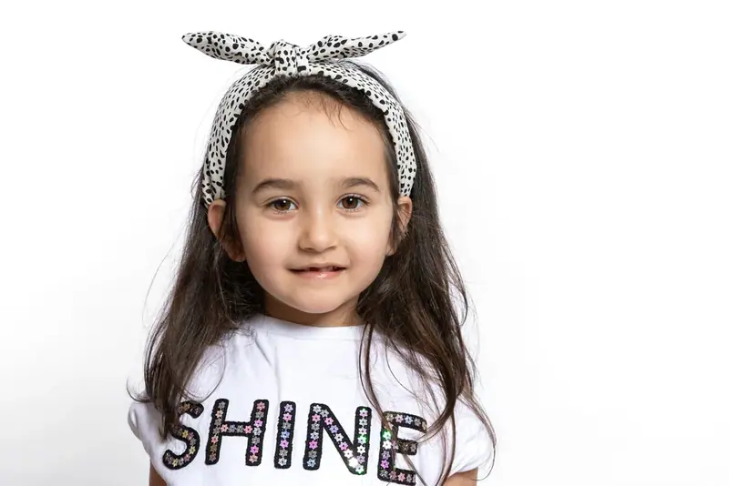 Girl in a headband and a white t-shirt with the word SHINE, white background