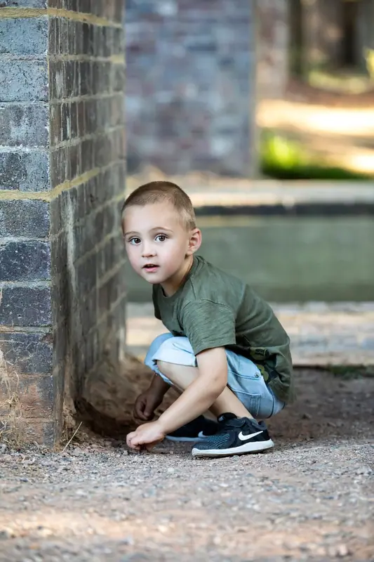 Boy in a green top crouching against a brick wall