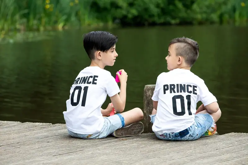 Two boys in matching t-shirts sitting on a jetty by a lake