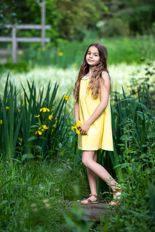 Girl in a yellow dress standing among reeds beside a wall