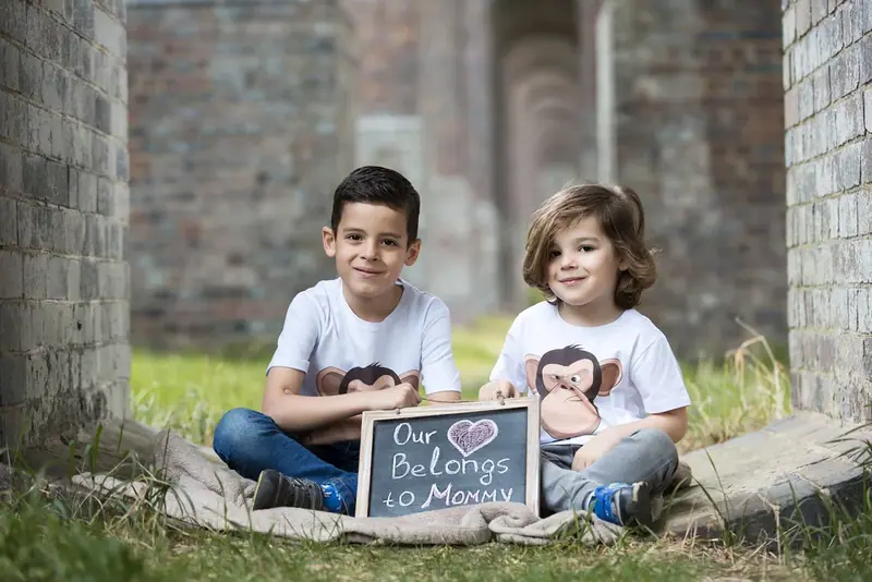 Two children sitting on the grass holding a small chalkboard sign