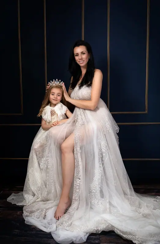 Mother in a long white dress with her young daughter in a dark studio