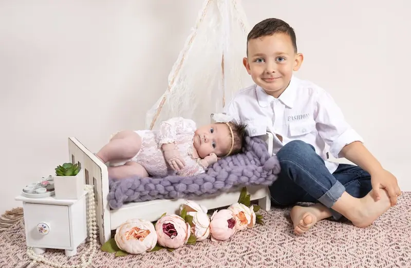 Boy lying beside his newborn sibling in a small wooden bed with flowers