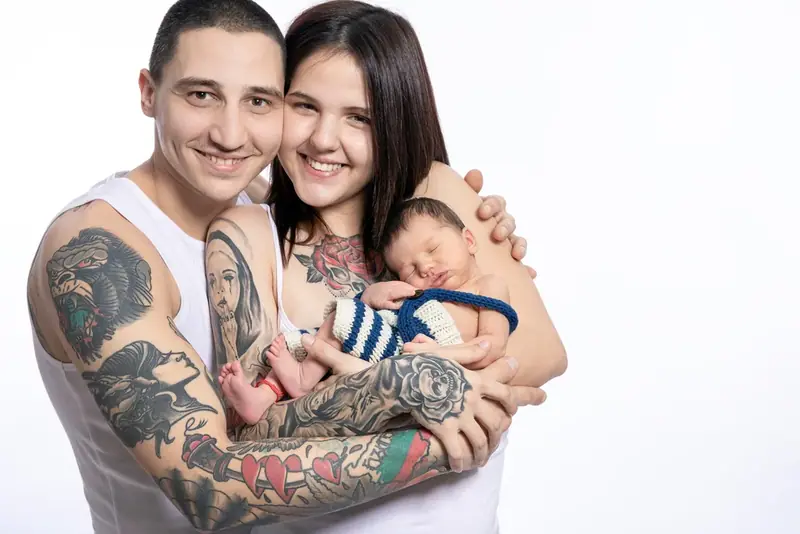 Parents holding a newborn, the father with tattooed arms, white background
