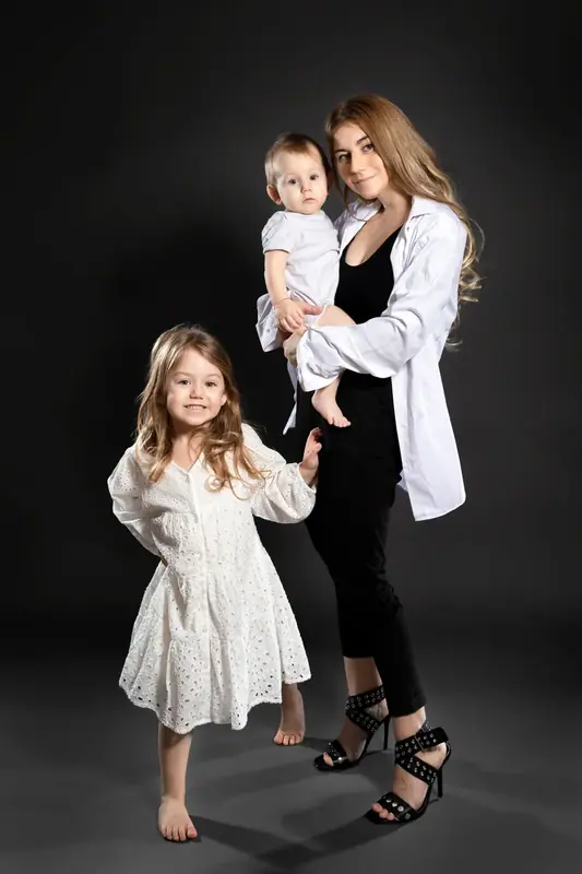 Mother holding a baby with a young daughter beside her in a dark studio