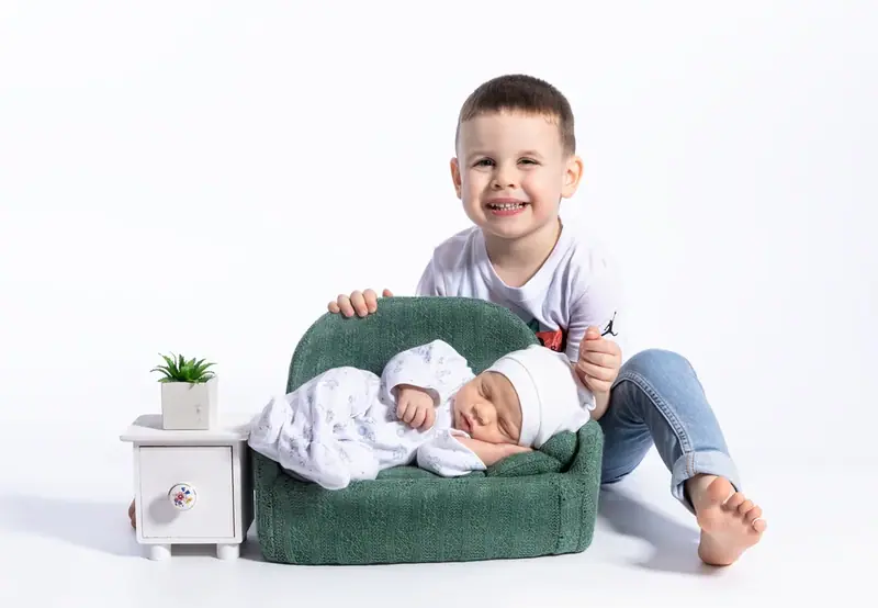 Boy sitting beside a sleeping newborn on a small green sofa