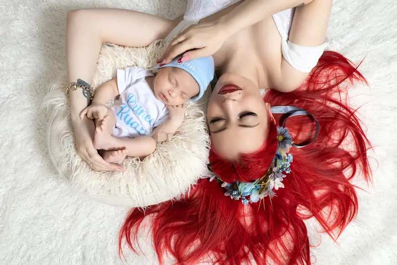 Mother with red hair lying head to head with a newborn on a white rug, seen from above