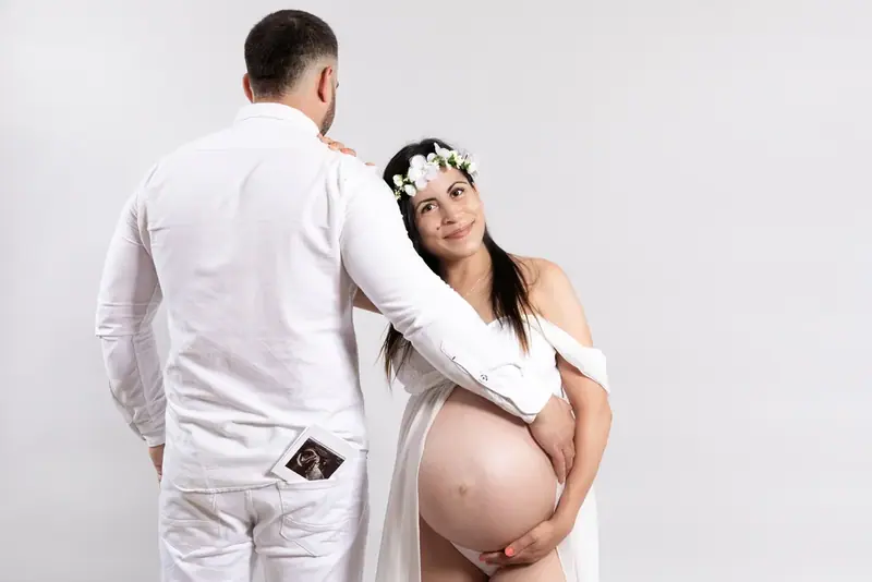 Expectant couple in white embracing, studio portrait