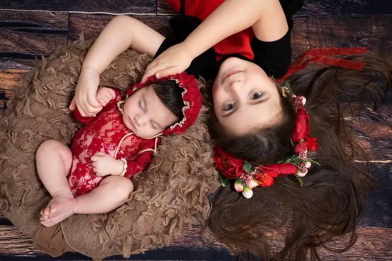 Mother and baby in red outfits lying head to head on a fur rug, seen from above