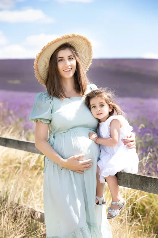 Expectant mother in a hat holding her young daughter by a lavender field