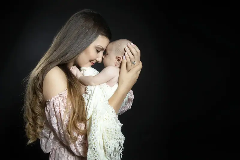 Mother cradling a newborn against a dark studio background