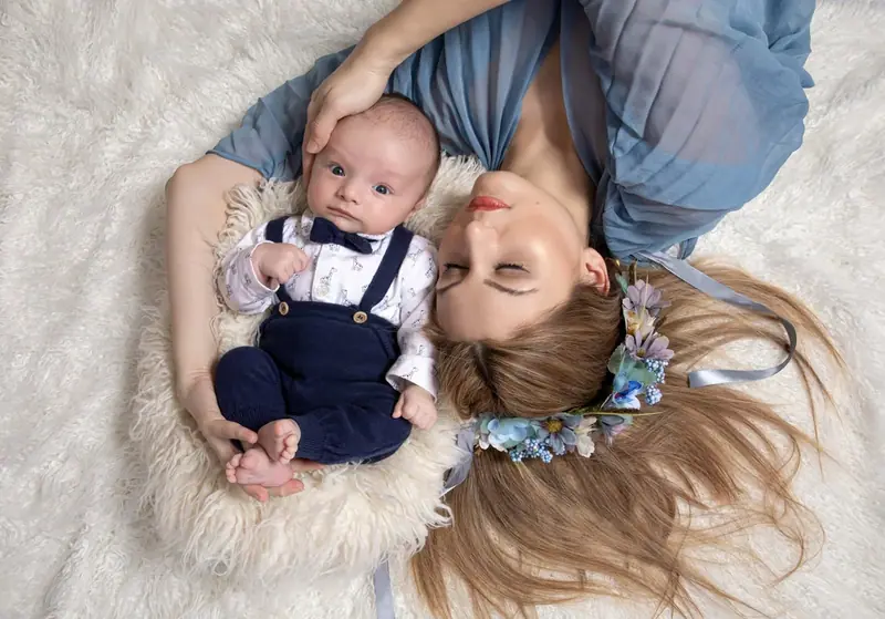 Mother lying head to head with a newborn on a white rug, seen from above