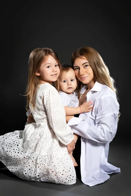 Mother with two young daughters in white, dark studio portrait