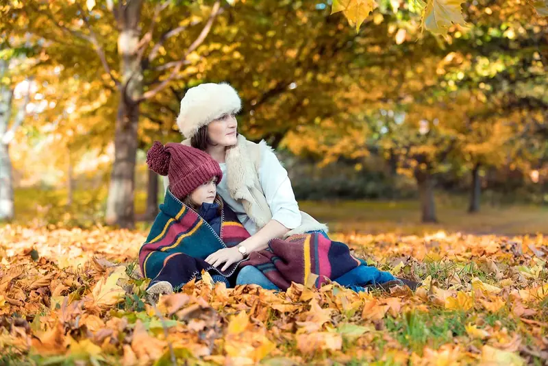 Family sitting among autumn leaves under golden trees