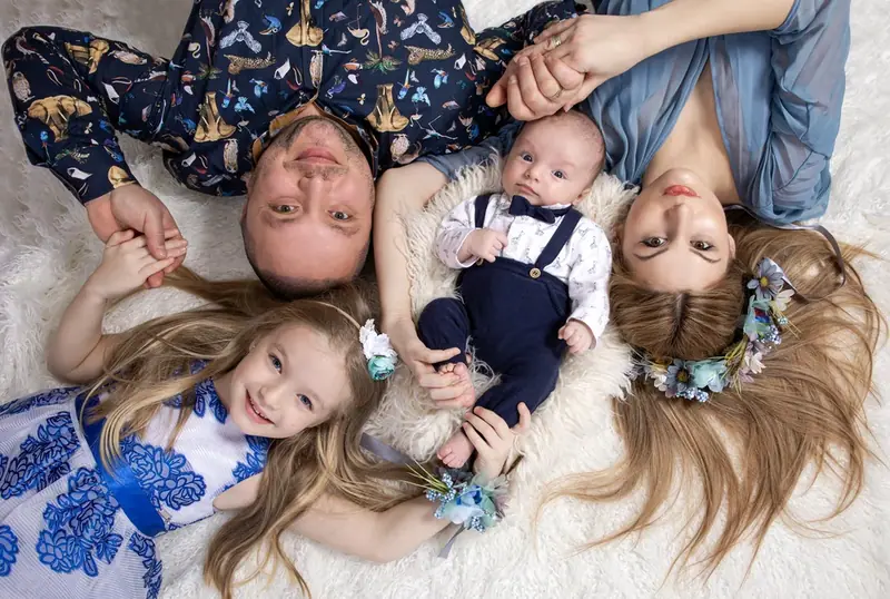 Family of four lying head to head with a baby on a white rug, seen from above