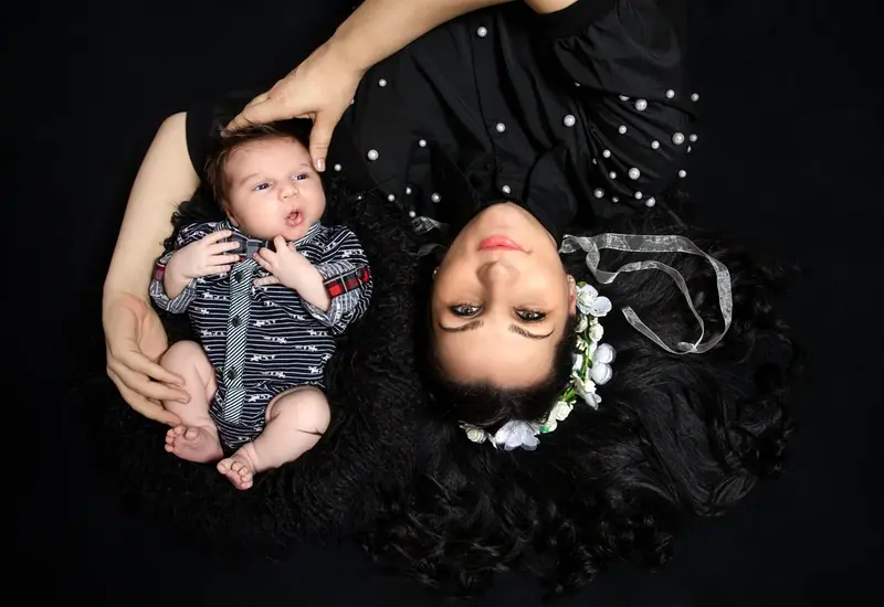 Mother in black lying head to head with a newborn, seen from above