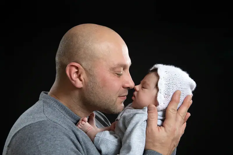 Father holding a baby face to face, dark studio portrait