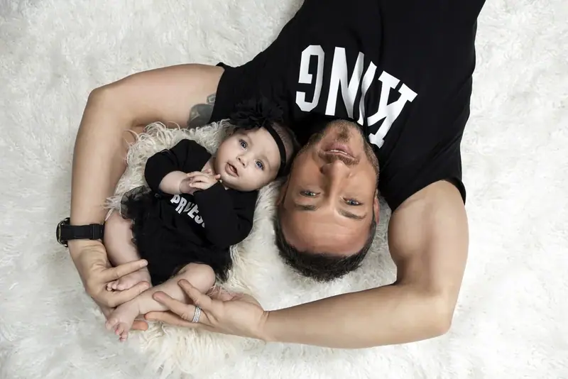 Father and baby in matching black t-shirts lying head to head on a white rug