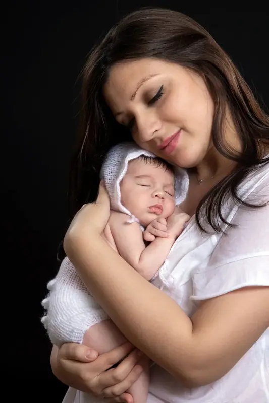 Mother in white cradling a newborn against her shoulder