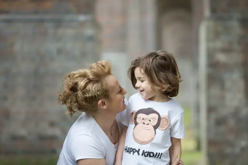 Mother and young son in matching t-shirts by a brick wall