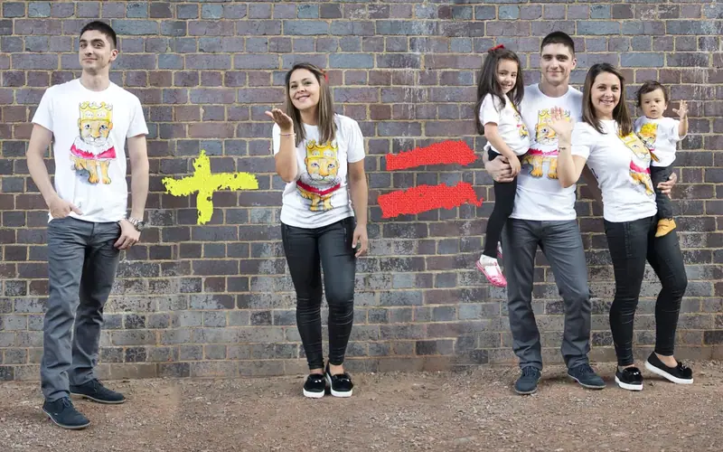 Family of four in matching t-shirts standing by a brick wall with painted symbols