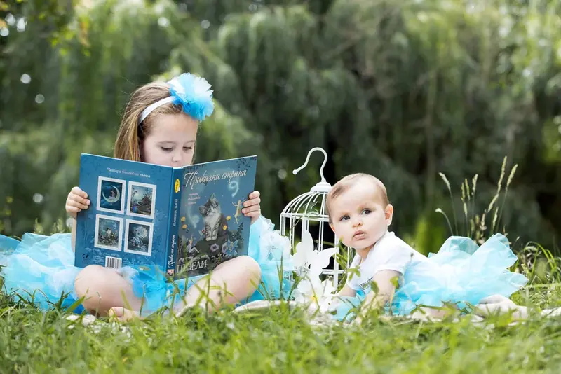 Two children in blue on the grass with a small photo frame and a birdcage
