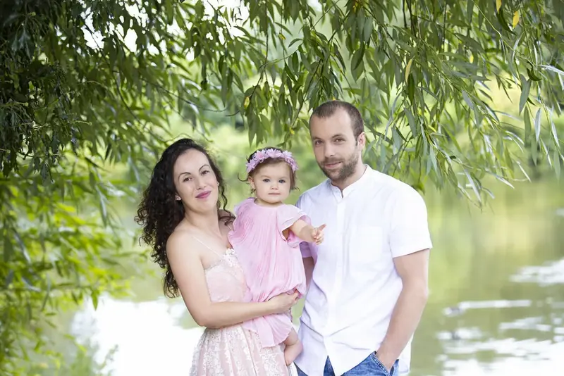 Parents and a small child sitting under a willow tree by a river