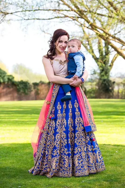 Mother in a blue and pink embroidered dress holding a toddler on a lawn