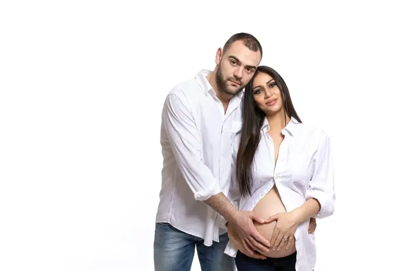 Expectant couple in white shirts, studio portrait on white
