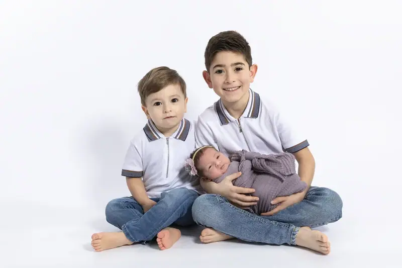 Two brothers sitting either side of a newborn on a white backdrop
