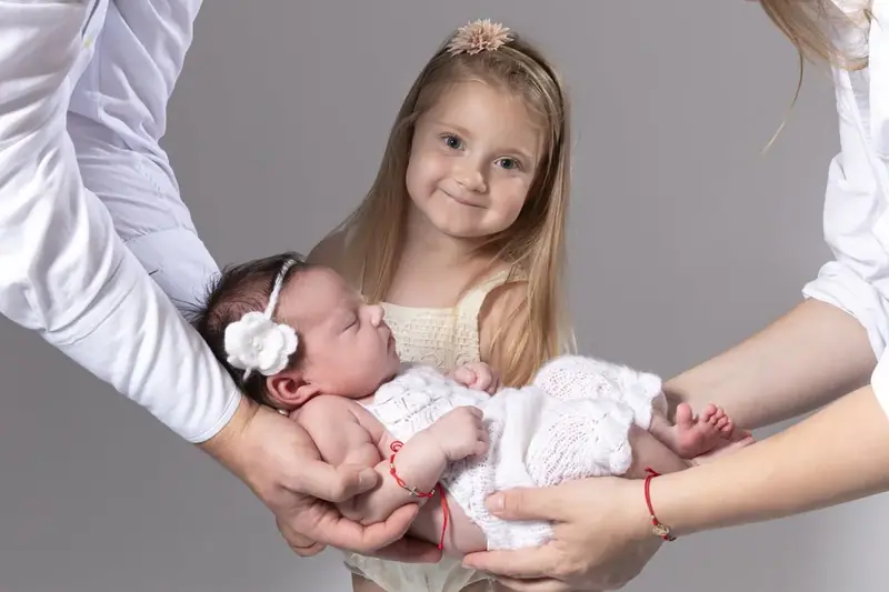 Two girls holding a sleeping newborn wrapped in white